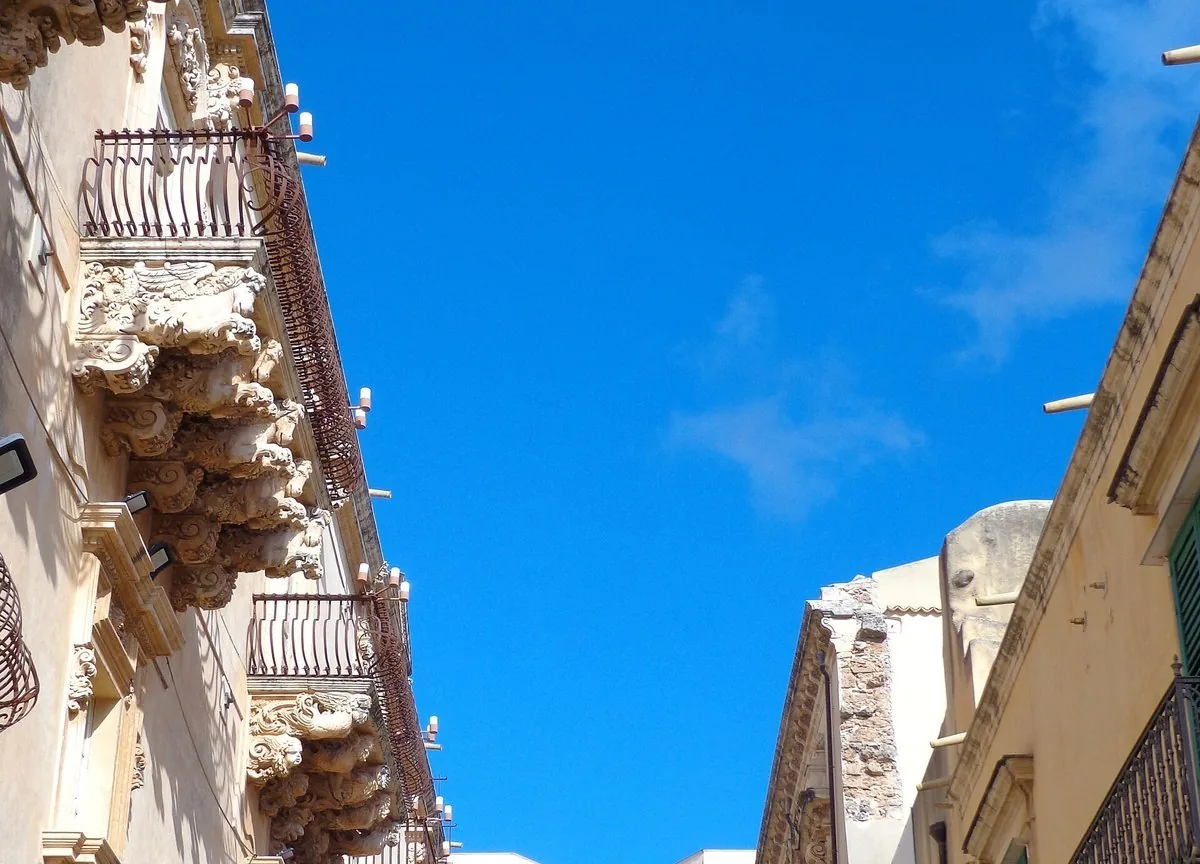 Una via barocca di Noto in pietra chiara, chiusa in fondo dalla facciata di una chiesa